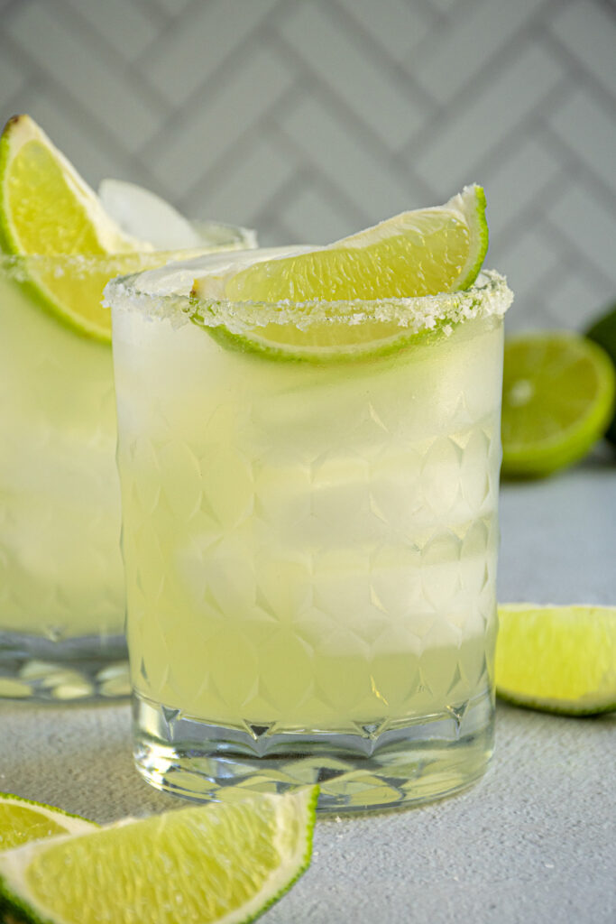 A rocks glass with a salted rim and a lime wedge filled with ice and a mocktail margarita. 