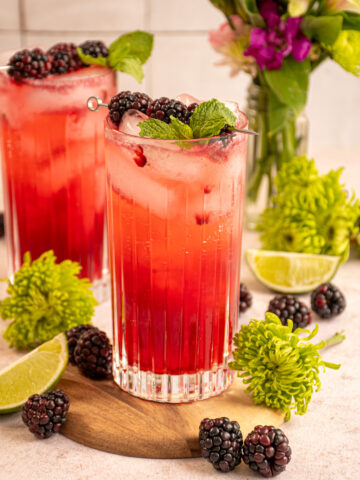 Highball glasses with ice and blackberry mojito mocktail topped with fresh mint and a skewer of blackberries.