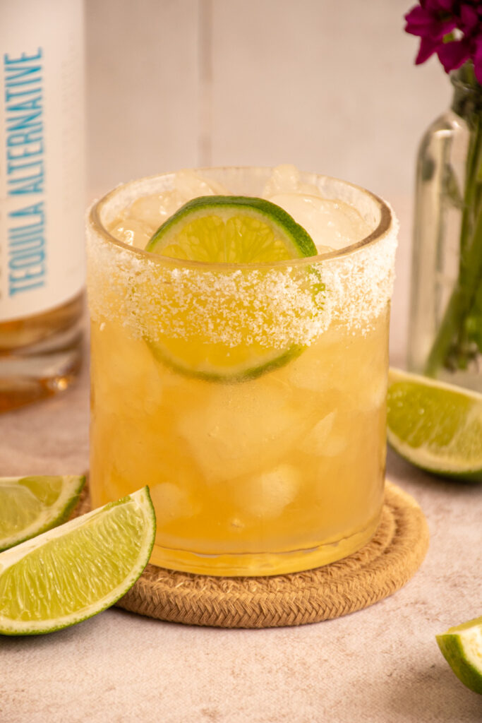 A glass with a salted rim filled with ice and ritual zero proof margarita with a lime slice.