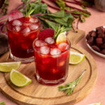Glass of dark red colored beet margarita garnished with beets, rosemary, and lime.