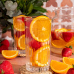 Glass of orange strawberry infused water with fresh strawberries and oranges.