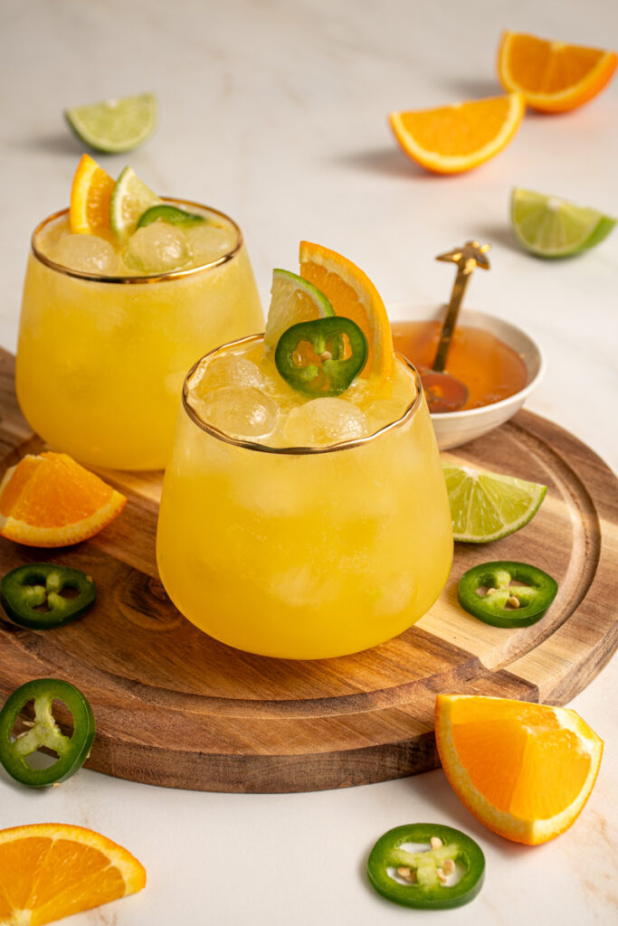 A glass with yellow colored Jalapeño Orange Margarita garnished with orange slice, lime slice, and jalapeno slice.