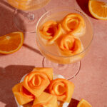 A small bowl and coupe glass with orange rose ice cubes.
