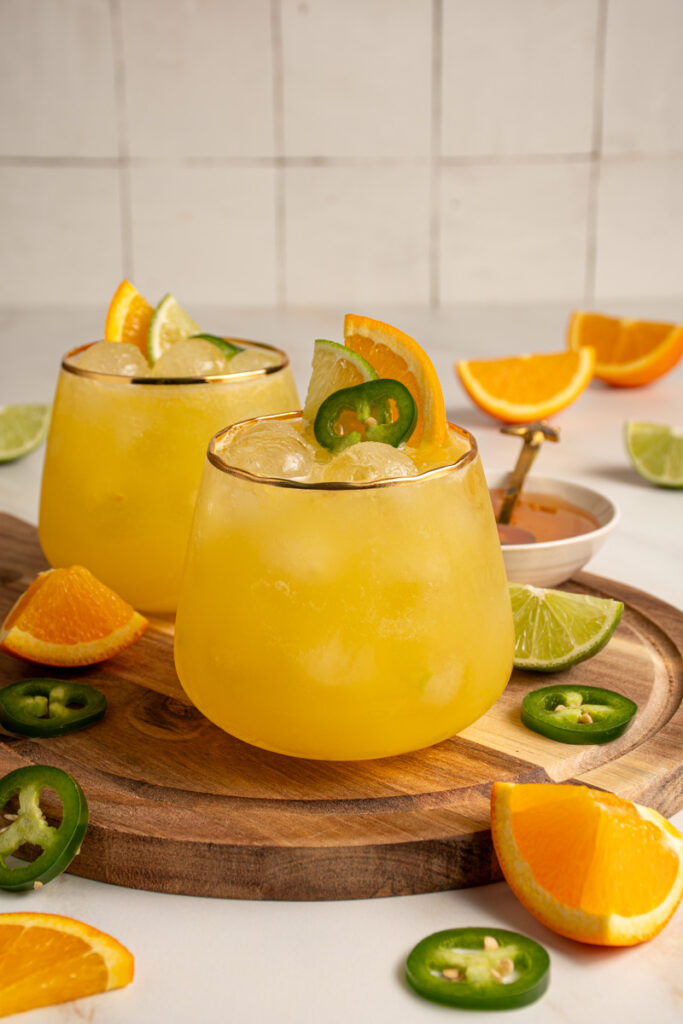 A glass with yellow colored Jalapeño Orange Margarita garnished with orange slice, lime slice, and jalapeno slice.