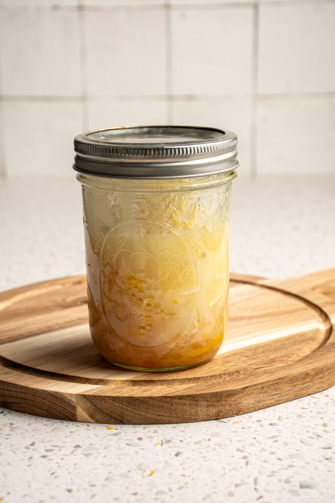 A jar with lid filled with sugar, lemons, and ginger.