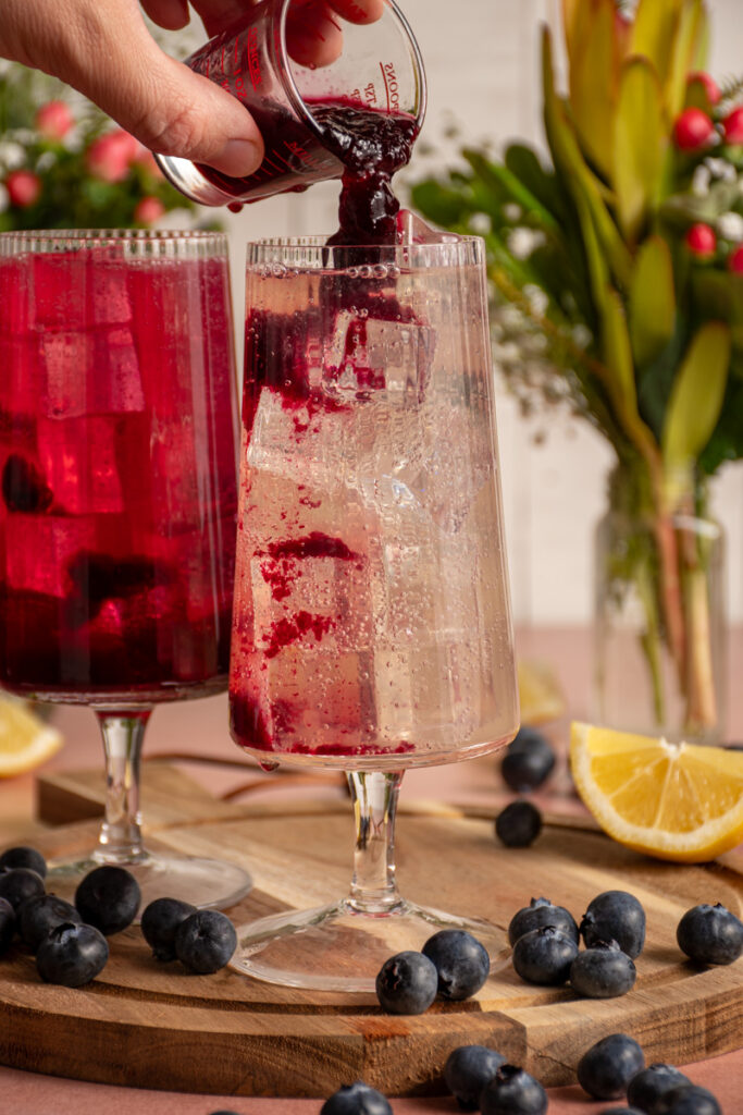 Adding blueberry syrup to a glass of ginger beer.