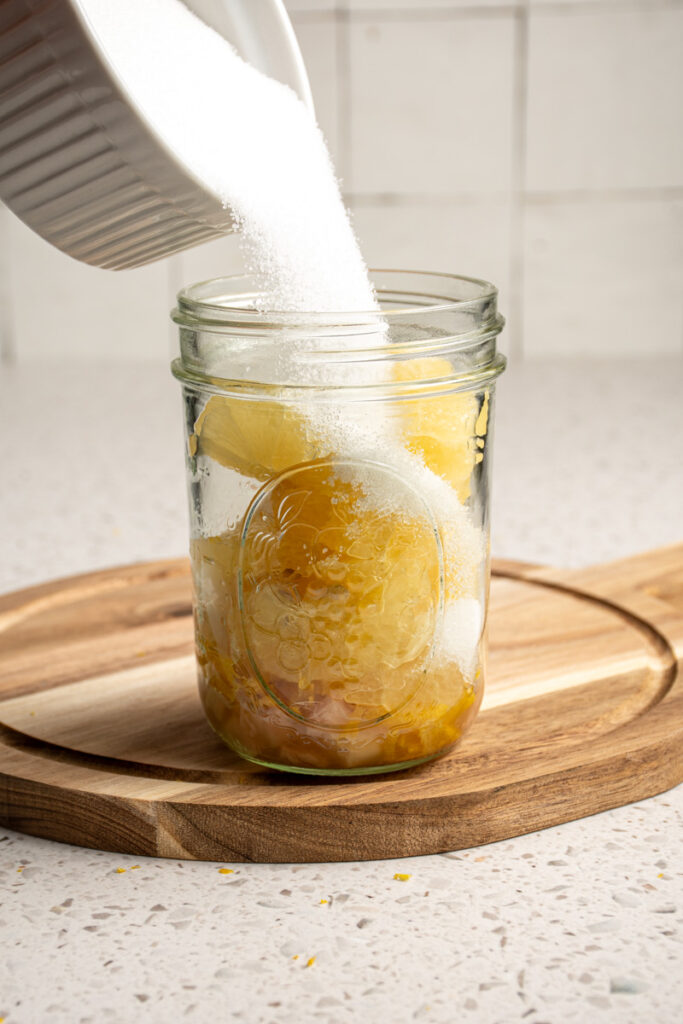 Pouring sugar into a jar with lemons.