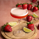 A coupe glass with tequila aperol cocktail with a strawberry garnish.