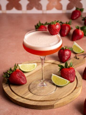 A coupe glass with tequila aperol cocktail with a strawberry garnish.