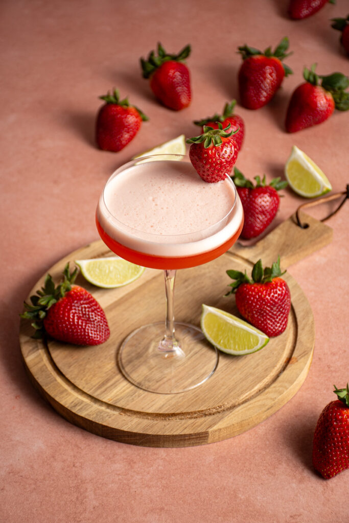 A coupe glass with tequila aperol cocktail with a strawberry garnish.