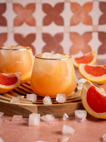 Stemless wine glass filled with grapefruit elderflower spritz surrounded by grapefruit slices.